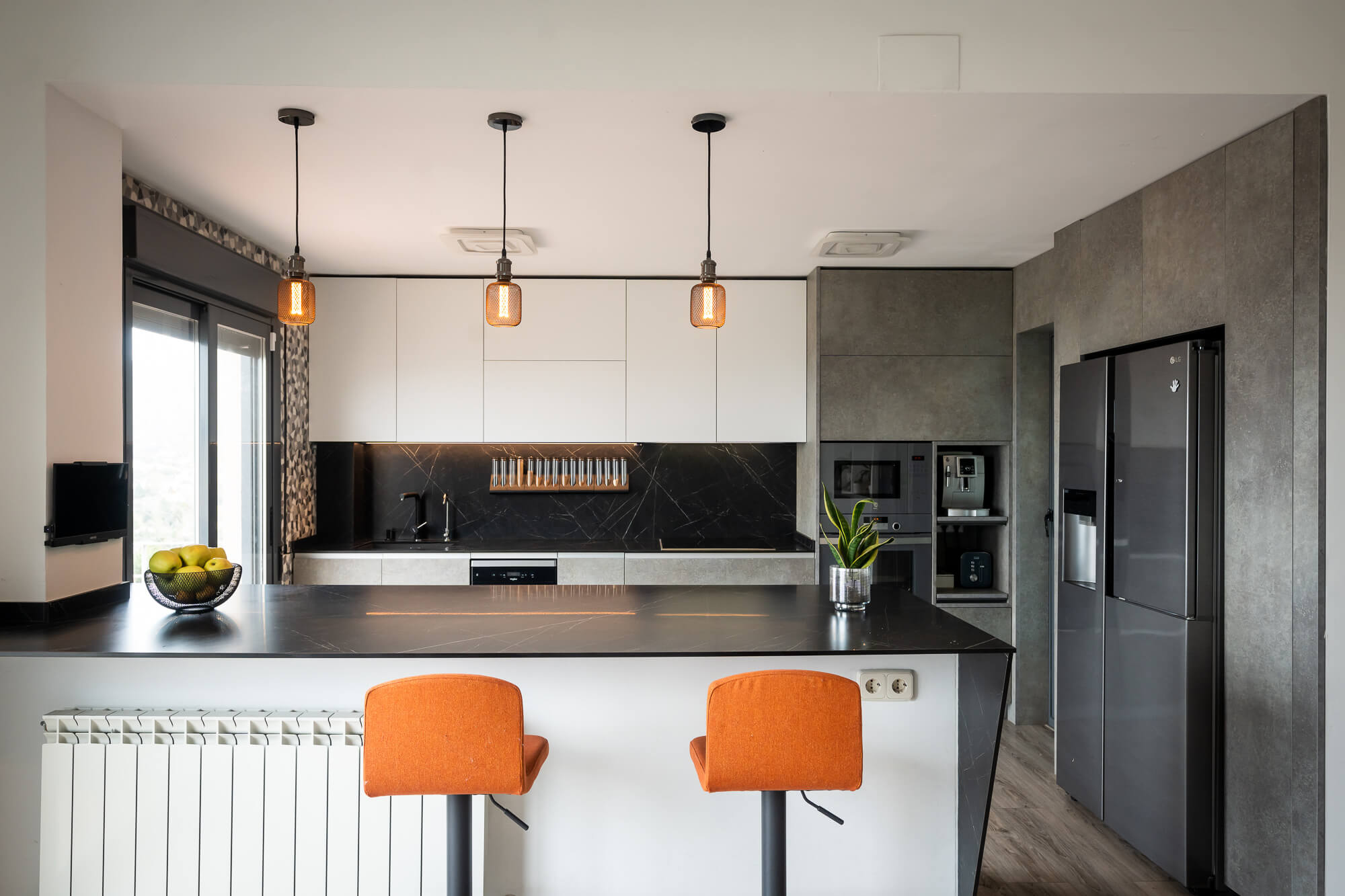 Cocina con isla y taburetes naranjas, muebles altos de madera y columnas oscuras con electrodomésticos integrados