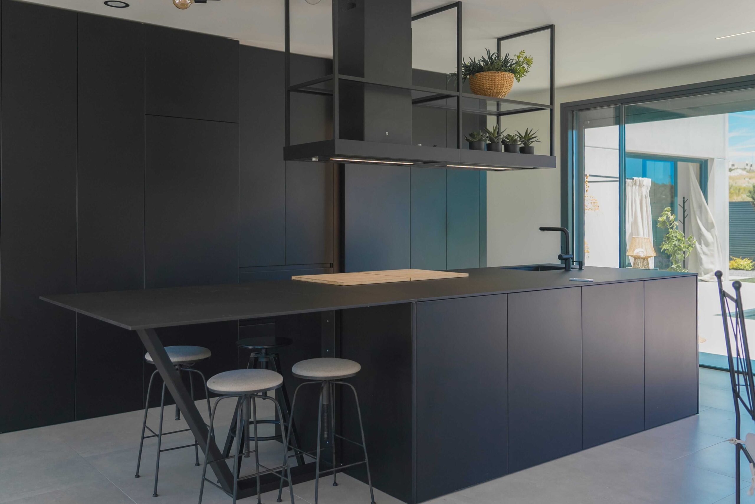 Cocina lacada en negro con isla central y campana suspendida, diseñada por Studio Drommen para una vivienda de Majadahonda