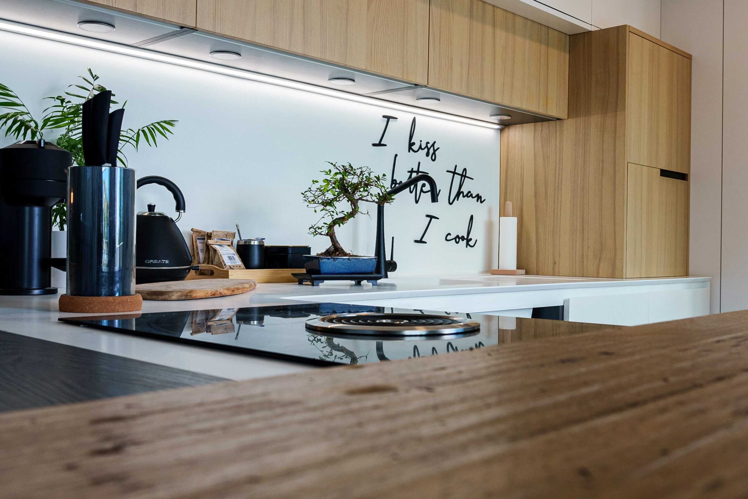 Cocina a medida con frentes de madera natural, placa de inducción y barra de madera maciza, diseñada por Studio Drommen