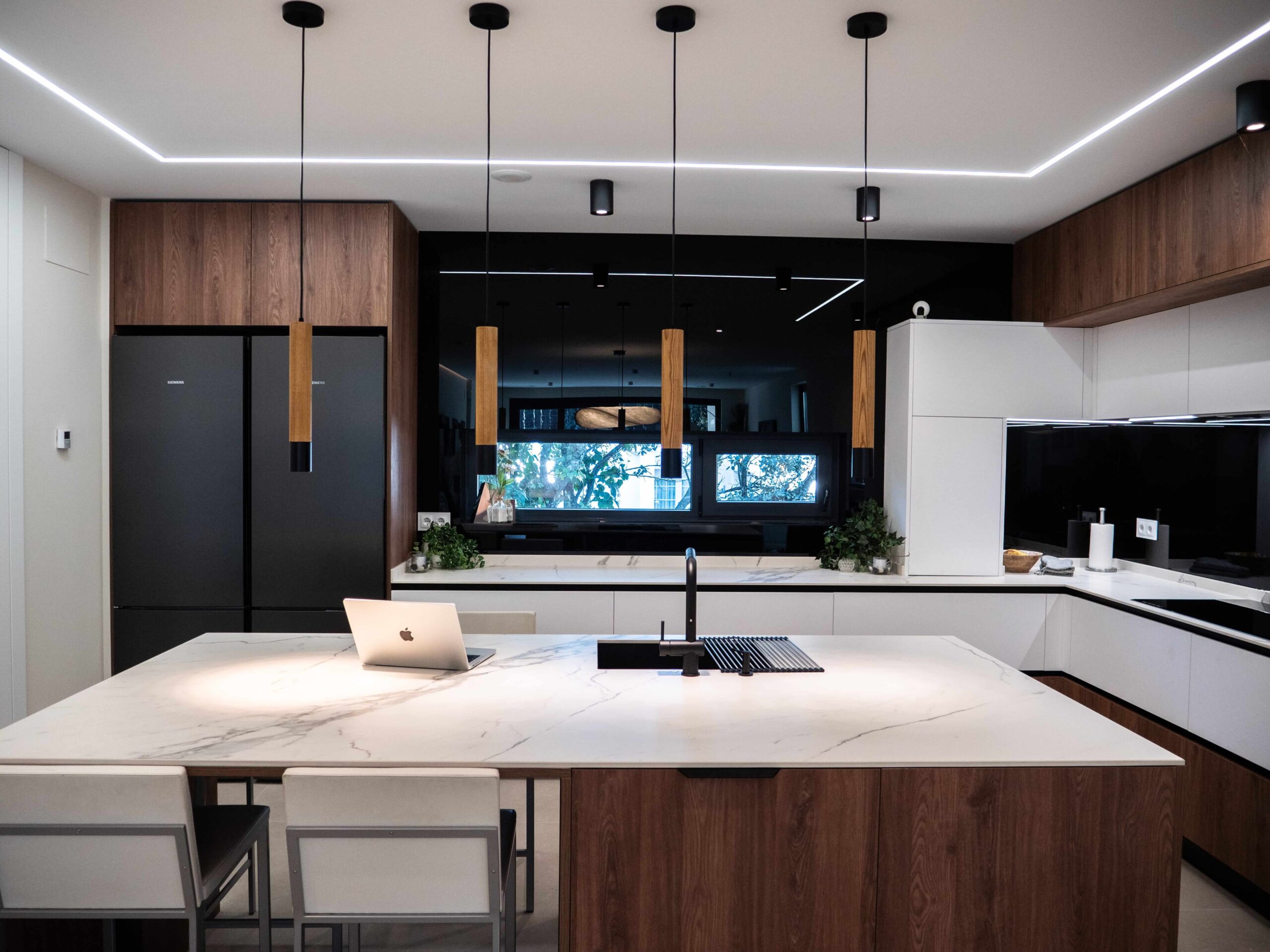 Cocina a medida con isla de encimera veteada, frentes de madera y columnas oscuras, diseñada por Studio Drommen