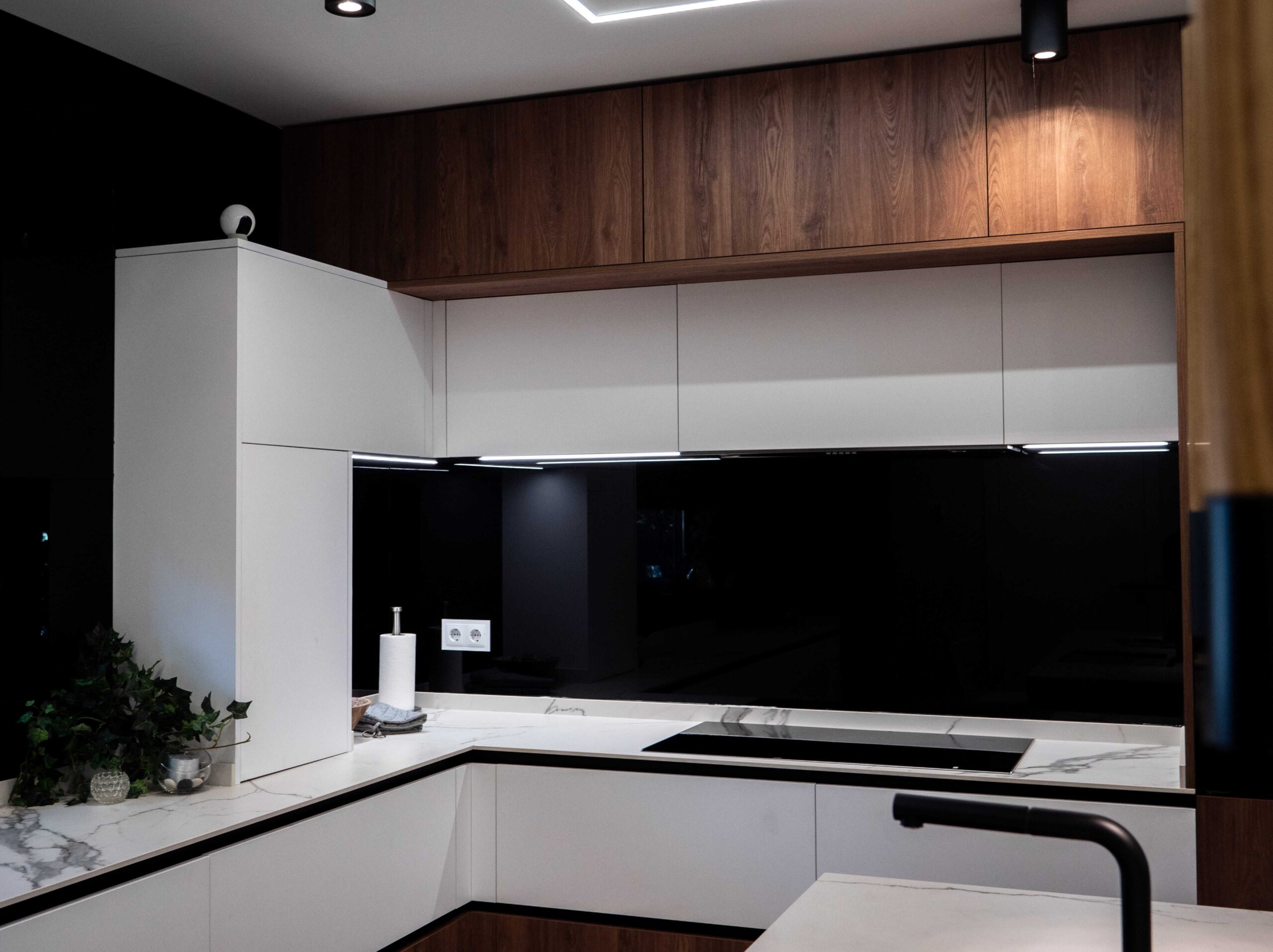 Cocina a medida con muebles altos de madera, frentes blancos, frontal negro y península con encimera clara